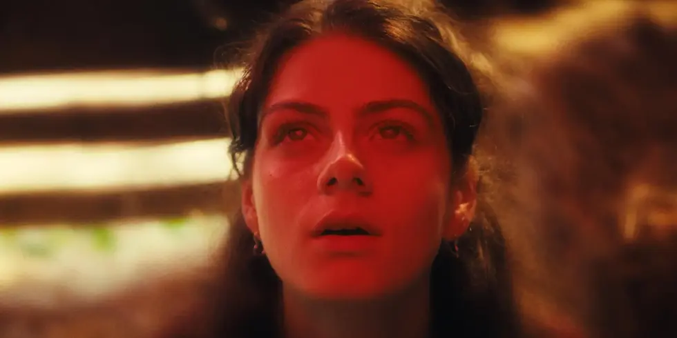 Szenenbild aus „Euphorie“: Rotes Licht erhellt das Gesicht von Derya Akyol als Mila, die mit staunendem, zugleich entrücktem Blick nach oben schaut