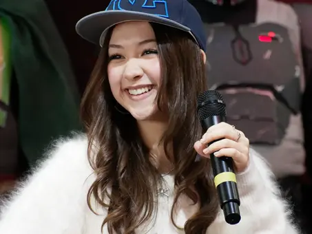 Kyriana Kratter lächelt mit Mikrofon auf einer Bühne und trägt eine Baseballkappe – sie wurde für die Rolle von Lev in „The Last of Us“ Staffel 3 besetzt.