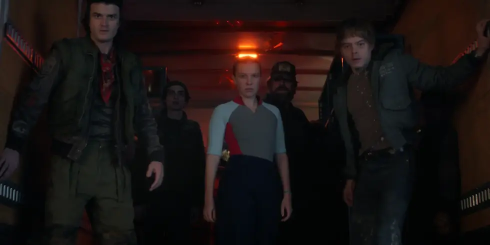 Szene aus der Netflix-Serie „Stranger Things“: Mehrere jugendliche Figuren stehen in einem dunklen, rot beleuchteten Gang und blicken angespannt nach vorn.