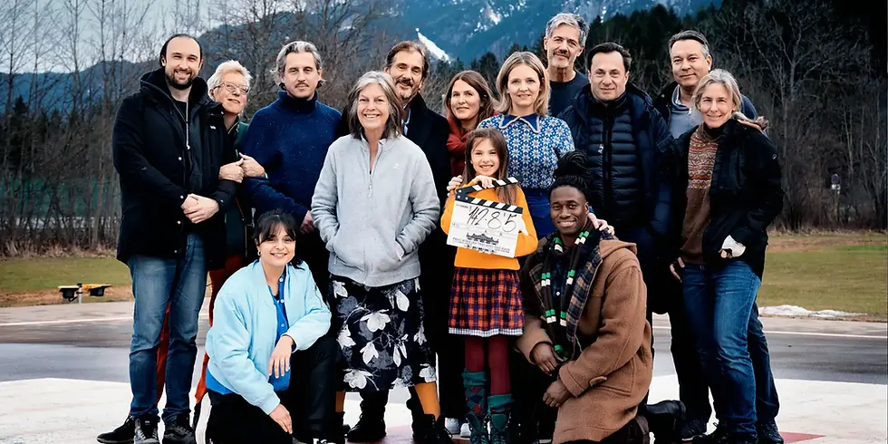 Gruppenfoto des Filmteams von „Frau Winkler verlässt das Haus“ nach Abschluss der Dreharbeiten: Rund 15 Personen stehen im Freien vor einer bergigen Landschaft, in der Mitte eine ältere Frau. Ein Kind hält eine Filmklappe in die Kamera. Das Ensemble posiert in winterlicher Kleidung auf einer asphaltierten Fläche.
