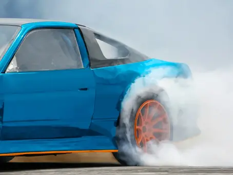 Symbolbild zu „Fast & Furious“: Ein blauer Sportwagen mit orangefarbenen Felgen lässt bei einem Burnout die Hinterreifen qualmen.