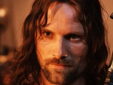 Viggo Mortensen als Aragorn in „Der Herr der Ringe - Die Rückkehr des Königs“ mit ernstem Blick, langem Haar und Bart, im warmen Licht, neben dem Griff seines Schwerts.