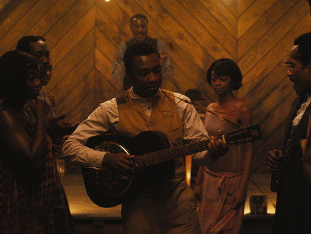 Eine Szene aus dem Film „Blood & Sinners“: In einem warm beleuchteten Juke Joint spielt ein Musiker mit Gitarre umringt von tanzenden und lauschenden Gästen.