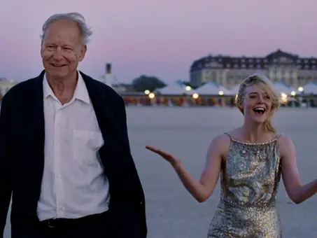 Stellan Skarsgård und Elle Fanning in „Sentimental Value“: Skarsgård geht lächelnd über einen weitläufigen Platz, während Fanning neben ihm in einem silbernen Kleid lacht und beide Arme ausbreitet. Im Hintergrund ist in der Dämmerung ein großes Gebäude zu sehen.