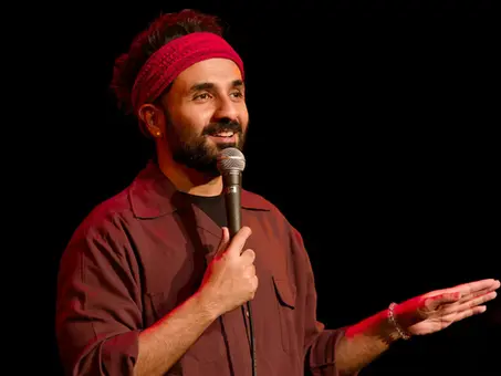 Vir Das bei einem Stand-up-Auftritt auf der Bühne mit Mikrofon in der Hand, aufgenommen unter rotem Bühnenlicht