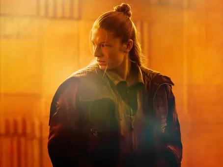 Szenenbild aus „Blade Runner 2099“: Eine junge Frau mit hochgebundenen Haaren und dunkler Jacke steht in orangefarbenem Licht und blickt angespannt zur Seite.