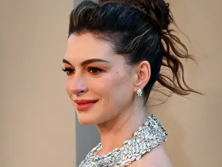 Anne Hathaway im Porträt bei einem öffentlichen Auftritt, mit hochgesteckter Frisur, funkelnden Ohrringen und silberfarbenem, mit Schmucksteinen besetztem Oberteil.