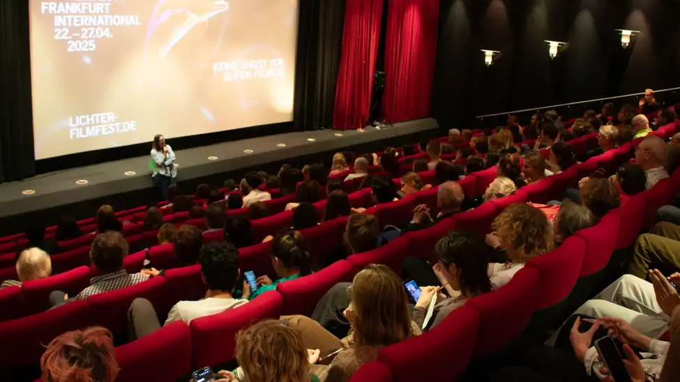 Publikum in einem voll besetzten Kinosaal beim LICHTER Filmfest Frankfurt während einer Filmvorführung mit Moderation vor der großen Leinwand.