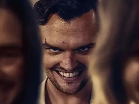 Promo-Motiv aus dem Horrorfilm „Smile 2 – Siehst du es auch?“: Ein Mann mit einem unnatürlich breiten Lächeln blickt bedrohlich nach vorne, während zwei verschwommene Figuren im Vordergrund das Bild rahmen.