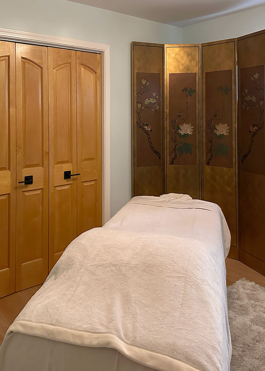 East West Oakland treatment room with calming cream colors, a Japanese screen and a massage bed in the centre of the room.