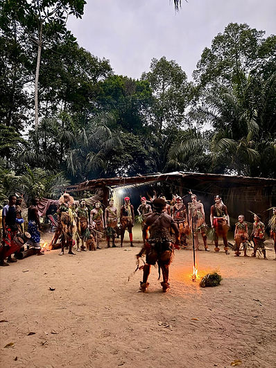 Danse rituelle en forêt: groupe en tenues de feuilles autour d’un feu, devant une hutte, ambiance sacrée.