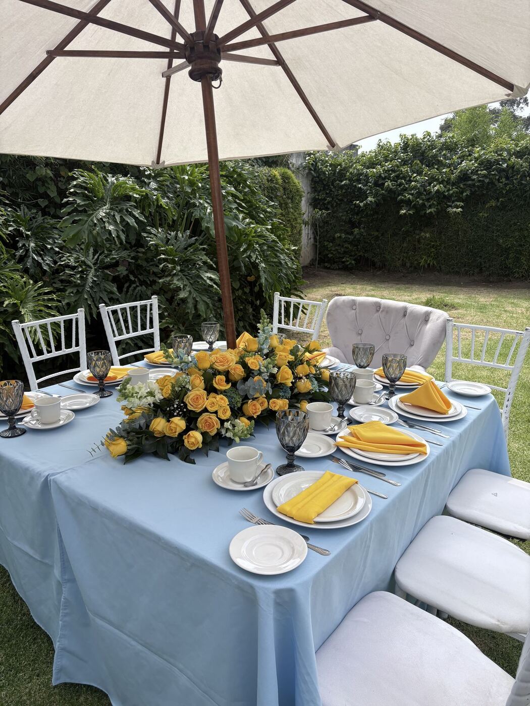 Mesa al aire libre con mantel azul y flores amarillas bajo sombrilla
