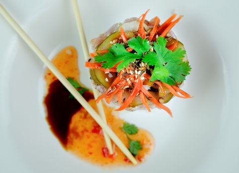 Sushi roll with chopsticks, carrots and sauce on a white plate