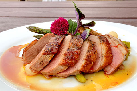Sliced duck breast with asparagus and sauce on a white plate