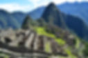 Iconic Macchu Pichu with stone buildings with no roofs green grass in the centre and tall mountains covered in thick green vegetation