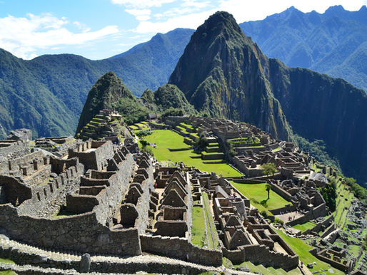 Ancient stone ruins of Machu Picchu with lush green terraces, set against a backdrop of towering blue mountains under a clear sky.