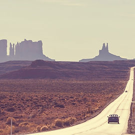 Paysage de désert ouest-américain avec une route menant vers des formations rocheuses de Monument Valley. Texte superposé : Explorez la vraie âme des villes américaines.