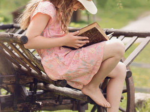 A girl with a hat on sitting in a summer garden reading a book
