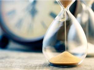 A close up of an hour glass with a clock in the background