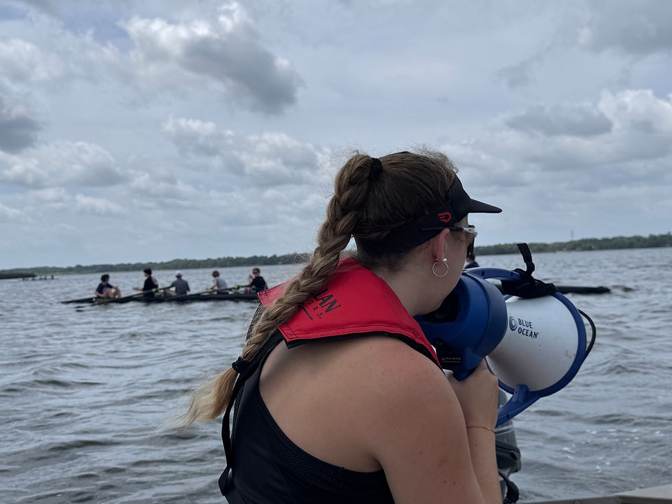 Coach Alex follows alongside a Learn2Row boat in the launch, using a megaphone to coach new rowers as they take their first strokes across Lake Jesup under dramatic Florida skies.
