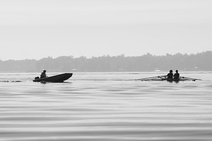 A SCAR coach follows alongside a rowing shell in a safety launch during a calm morning training session on the lake.