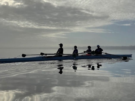 SCAR rowers practice on Lake Jesup at sunrise, rowing a four-person shell across calm water with dramatic cloud reflections in Seminole County, Florida.