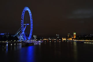 Photograph of the London Eye at night with the reflection in the sky and water.