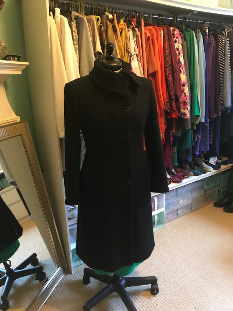 Black, smart, double breasted, mid length coat on a mannequin in front of a wardrobe