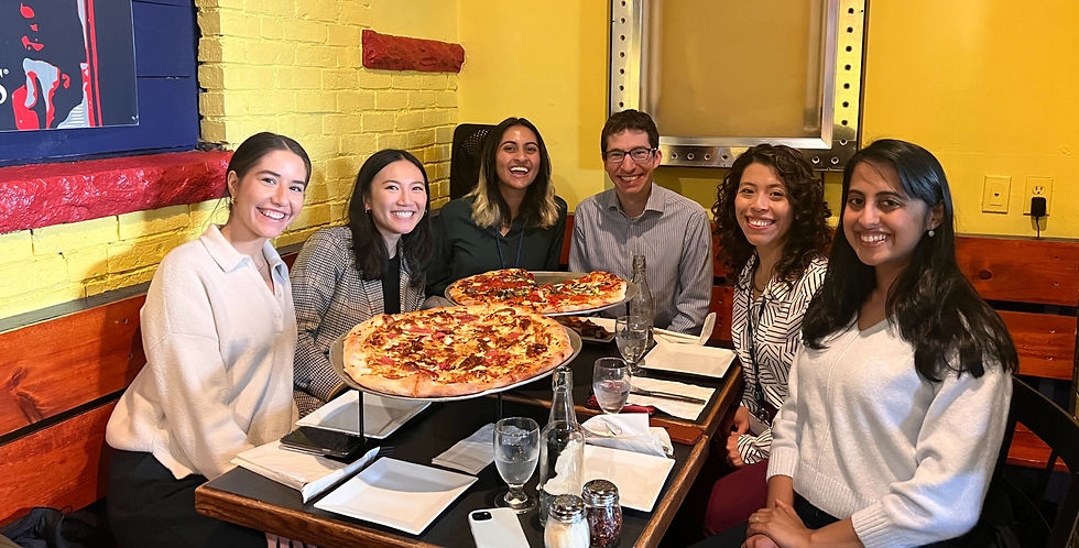 a group of 5 women and 1 man sit at a restaurant around a table that is serving pizza. They smile at the camera