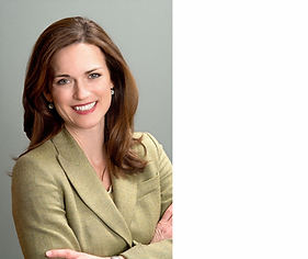 a woman with long brunette hair wears a sage green blazer and smiles while crossing her arms