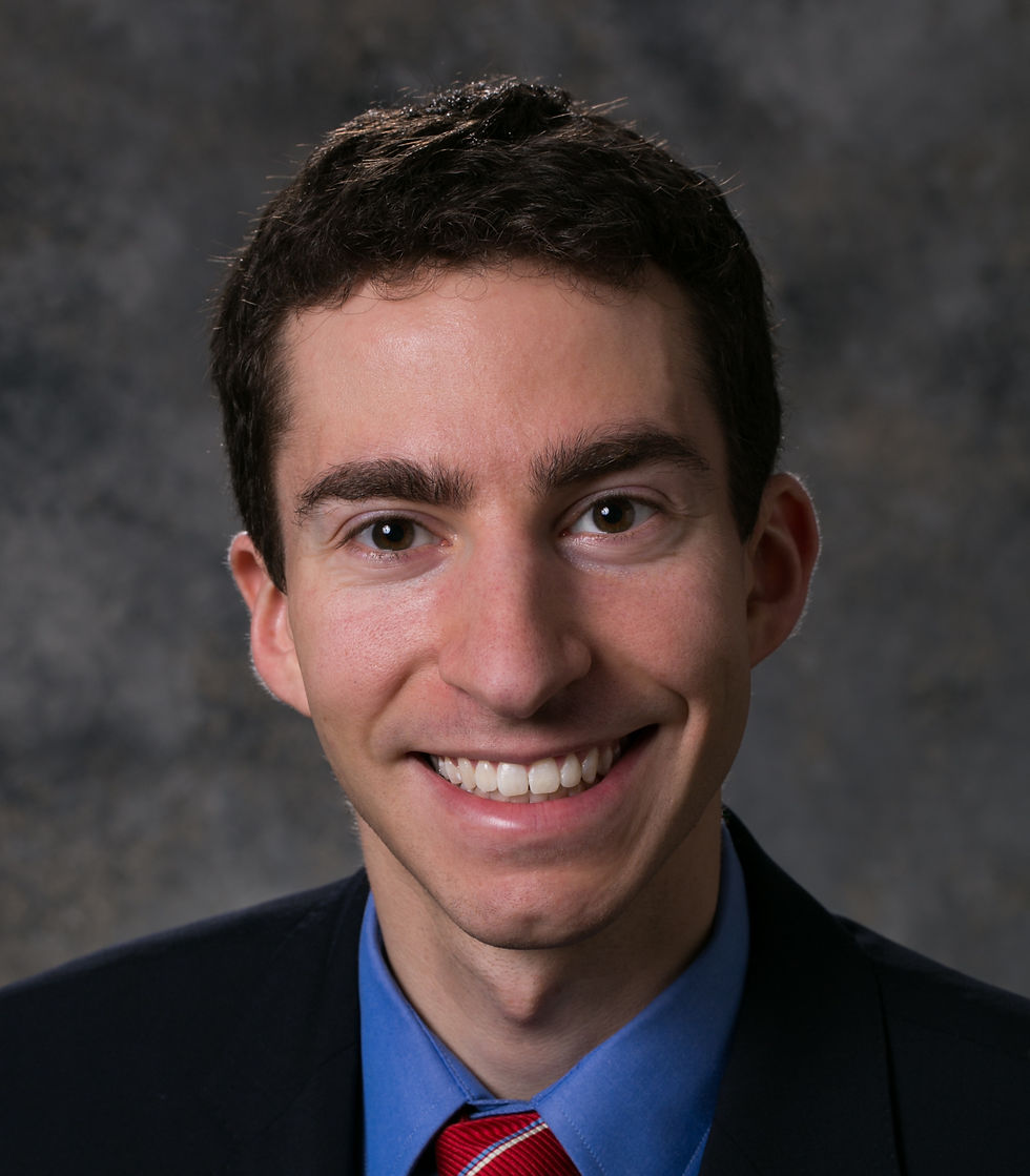 a white man with brown hair smiles in a headshot and wears a suit