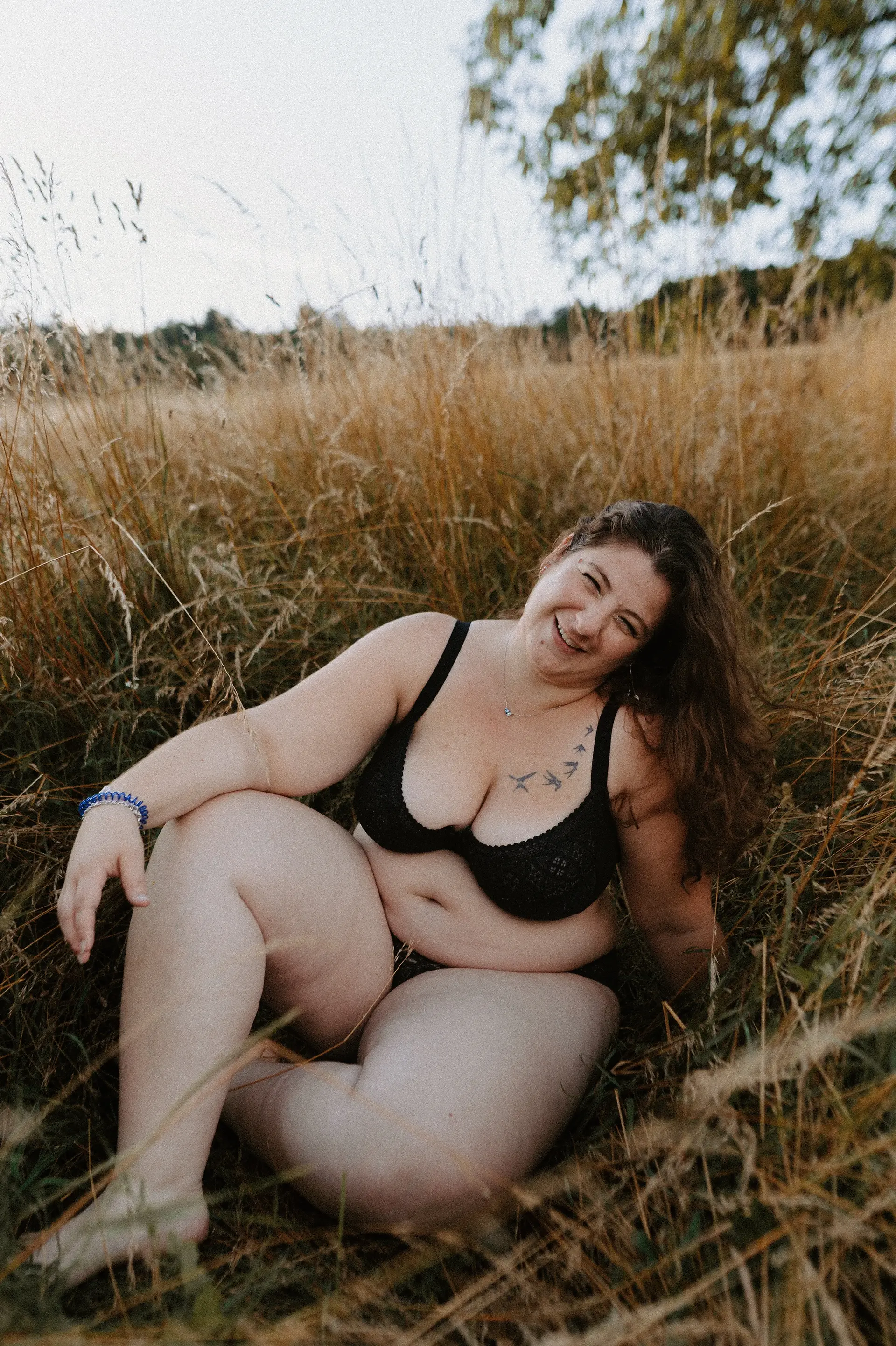 Femme souriante en sous-vêtements noirs, assise dans les herbes hautes, amandine-dirand