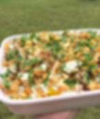 Dish with grilled chicken, diced potatoes, and fresh parsley on a creamy base, held outdoors with a grassy background.