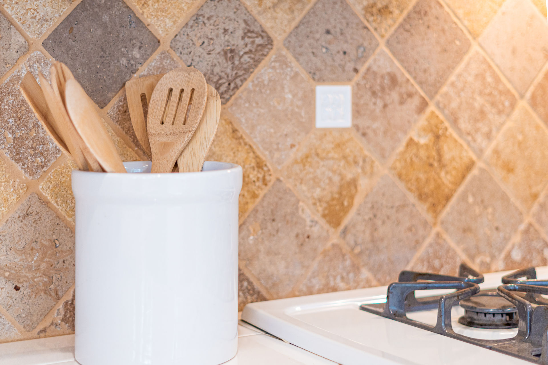 Jar filled with wooden cooking utensils on the counter beside the stove top