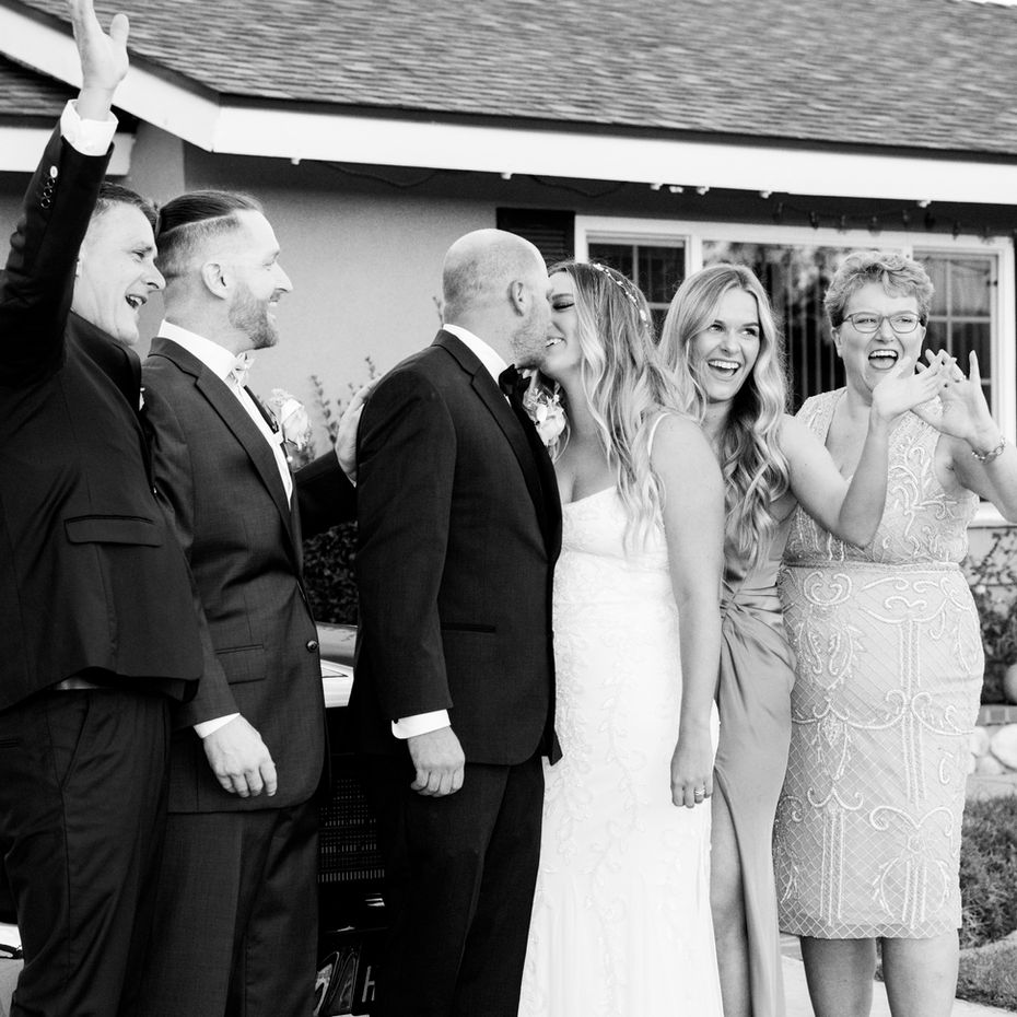 Wedding party looks at bridge and groom kiss. Black and white photo 