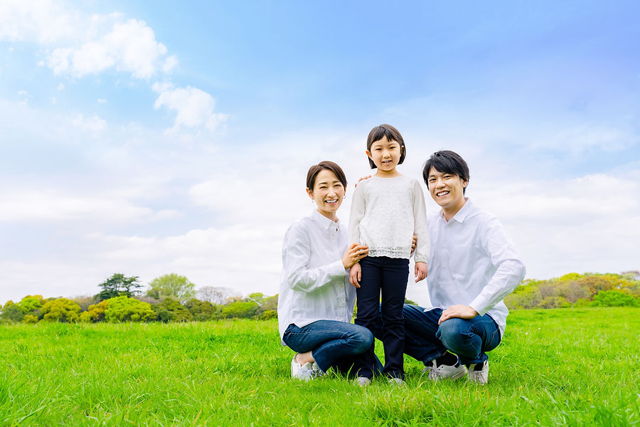 青空の下の草原で並ぶ笑顔の家族