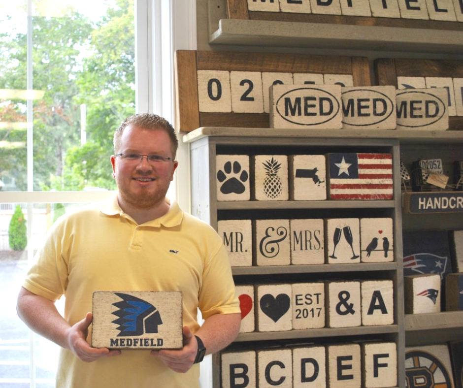 Young man smiles as he stands in front of shelves containing a selection of gifts.