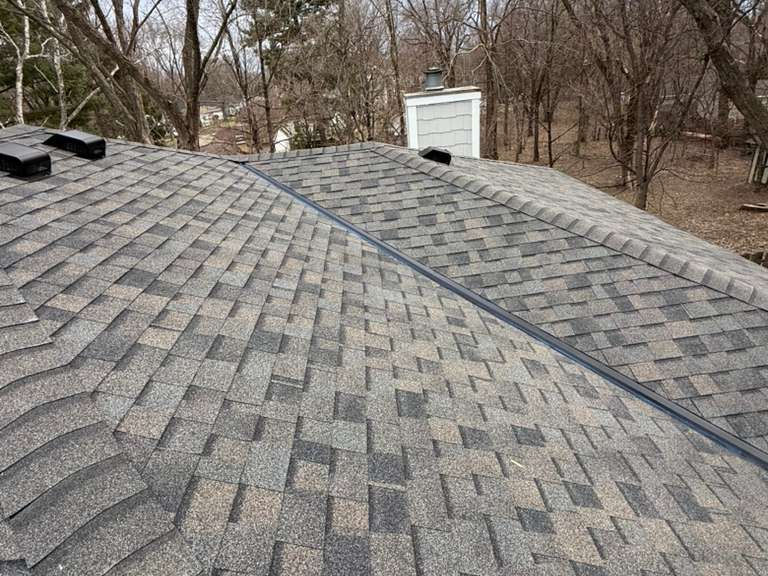 Minnesota home roof with gray asphalt shingles, ridge vent, and chimney inspected for possible storm damage by Lakeside Exteriors.