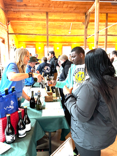 Woman pours drink from bottle for man at bustling indoor event.