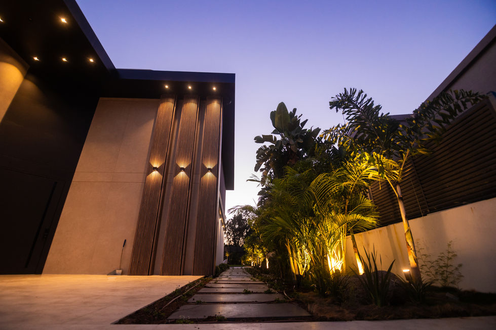 מבנה כניסה מוארת בשקיעה, שביל אבן עם צמחייה, אור צהוב, קו נקי - אור וירוק.