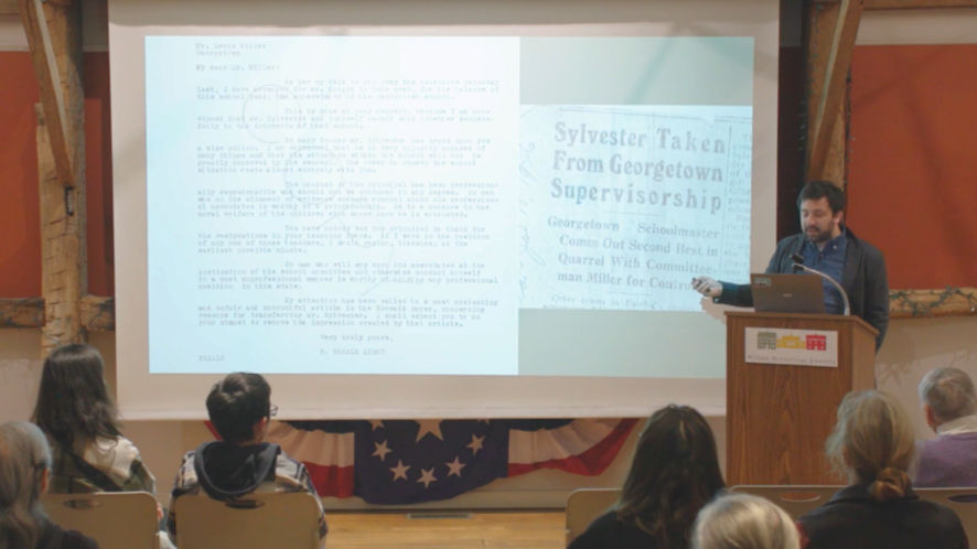 Historian presenting archival document and newspaper slide during recorded history lecture