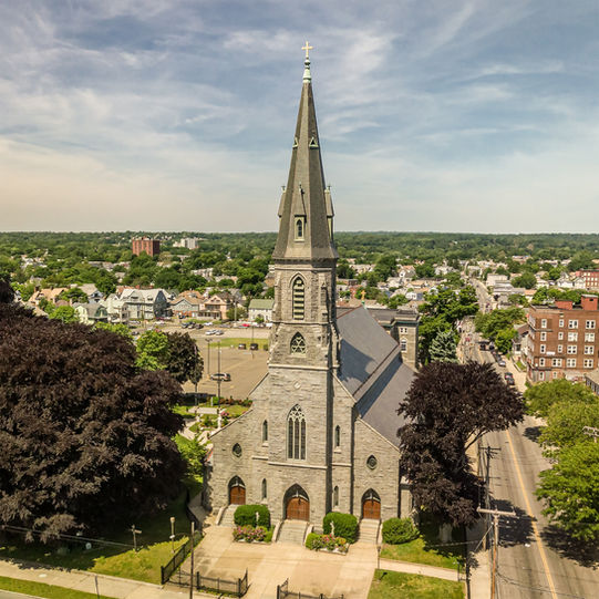 Aerial drone photo of Saint Augustine Cathedral church in Bridgeport Connecticut with tall stone steeple and surrounding neighborhood