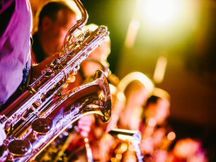 Close-up of a saxophone in a warm-lit jazz band, with blurred musicians in the background on stage.