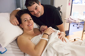 A mum holding her newborn baby in the hospital with her husband by her side in the hospital immediately after giving birth