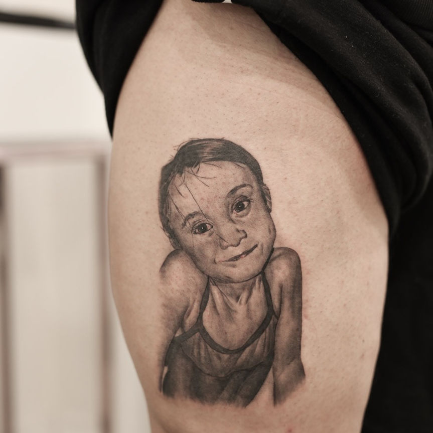 black and grey realism tattoo of a daughter portrait on the thigh