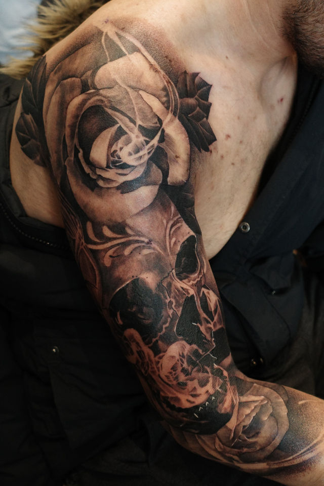 black and grey upper arm tattoo of a big skull and roses