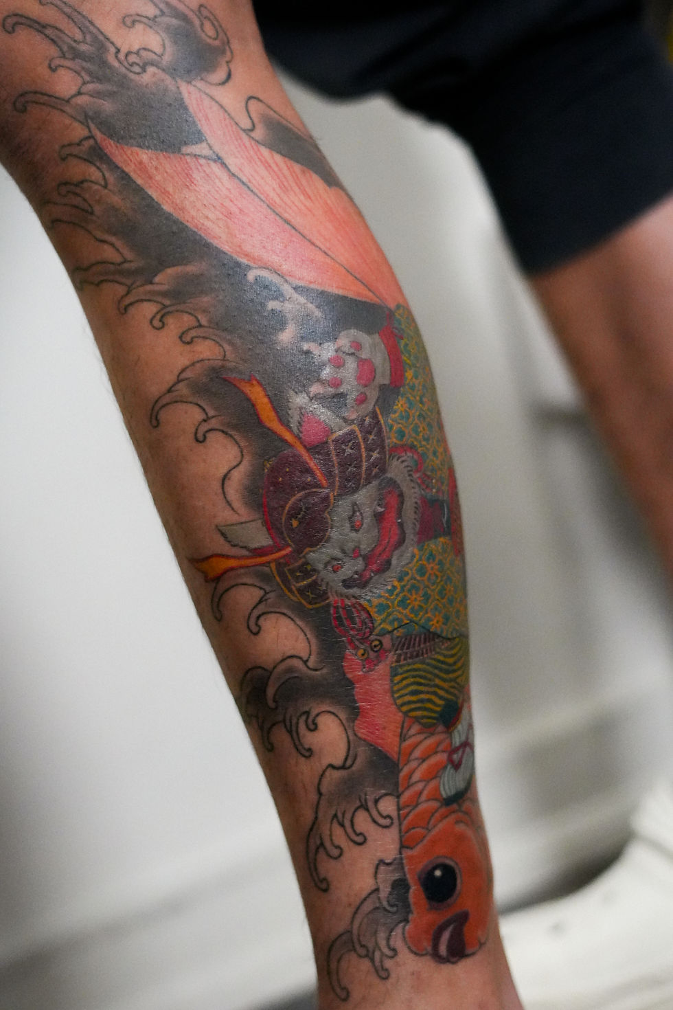 neo asian tattoo of a cat samurai killing a gold fish on a lower leg as part of a leg sleeve