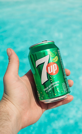 a hand holding a can of 7up by a pool_ed