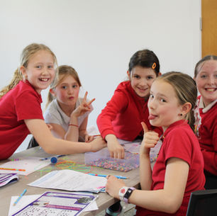 Group of five girls participating in a TECgirls workshop, smiling and playfully posing while working on a hands-on STEM activity with beads, string, and educational worksheets at a table.