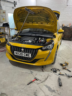 Yellow Peugeot 208 with front panels and bumper attached. Bonnet raised showing engine bay